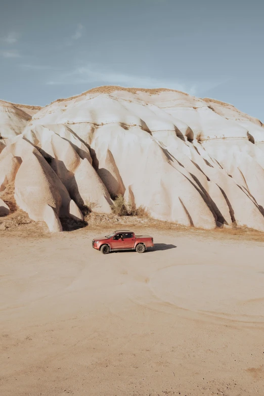 a truck parked in the sand in front of a huge rock wall