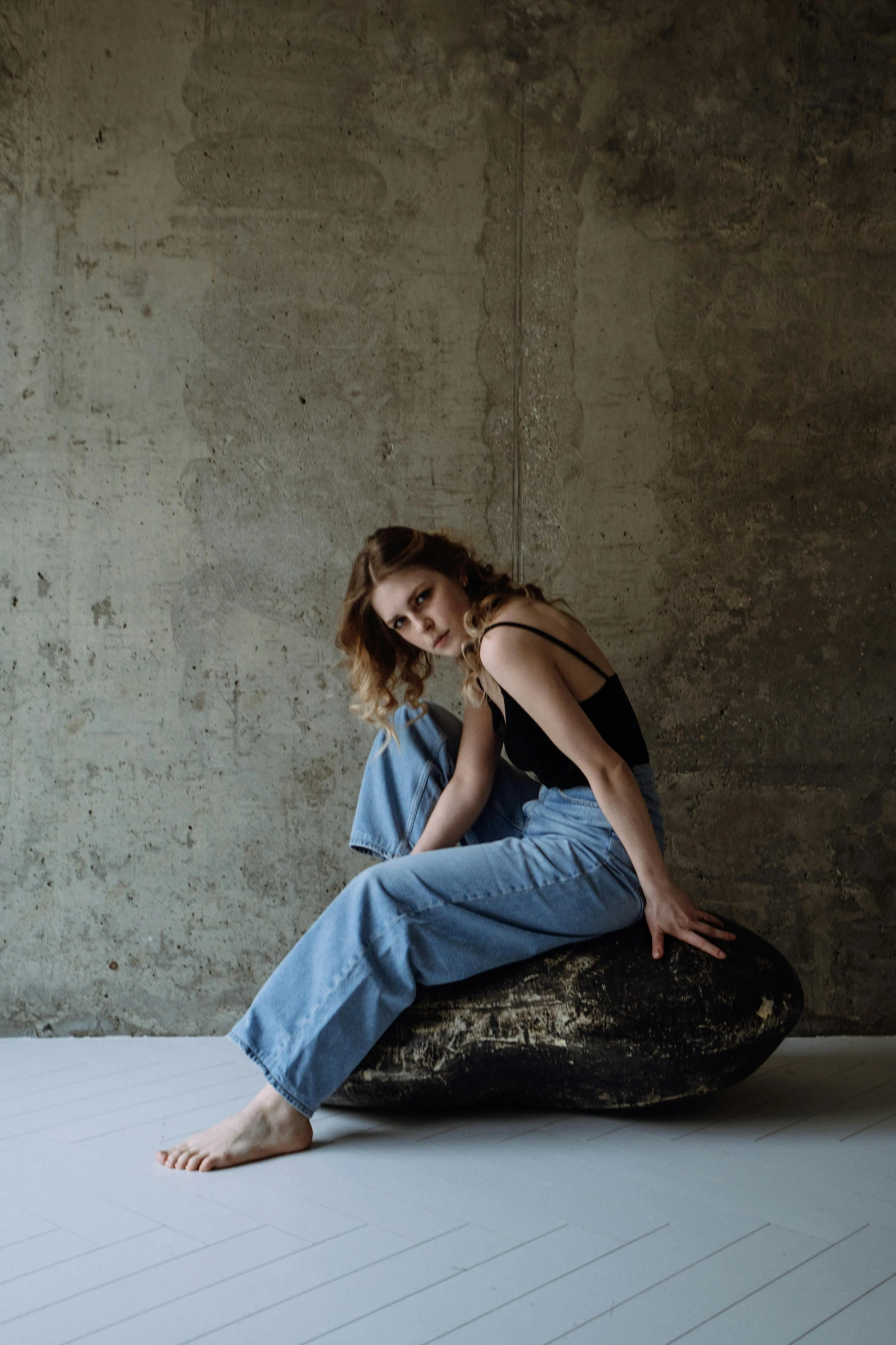 a girl in jeans sits on a rock and stares