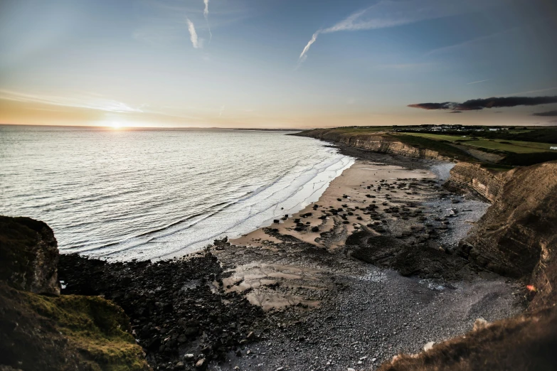 a sandy beach with waves breaking on it's shore and the sun peeking out behind the horizon