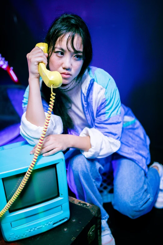 an asian woman is crouched down, holding a telephone and a vintage television