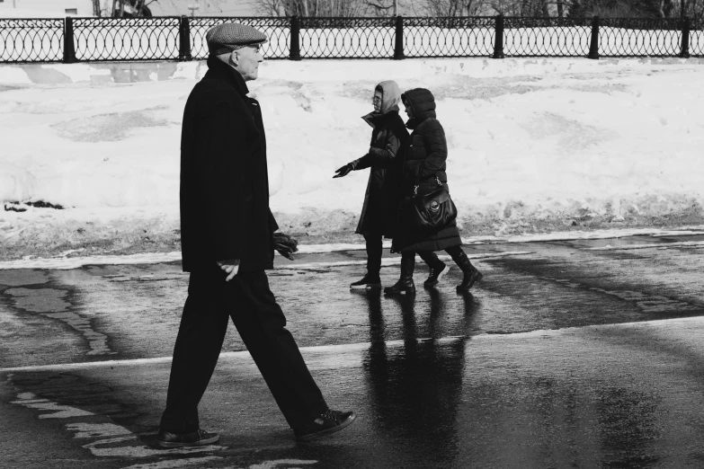 two men walk down a snow - covered street as two others cross the road