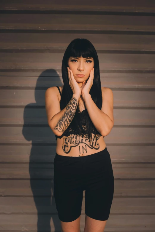 woman in lingerie with tattoos posing against gray wall