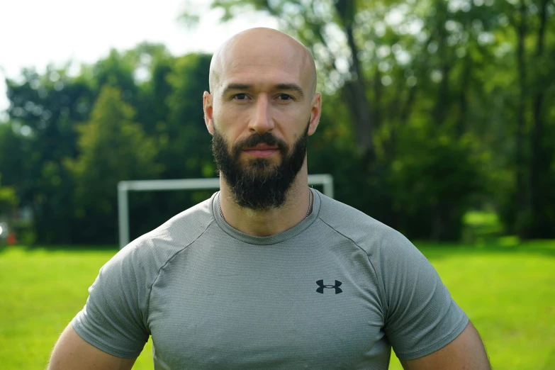 a man with a beard and gray shirt standing in a green field