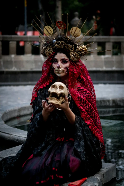 a woman wearing an elaborate head piece with a skull in her hand