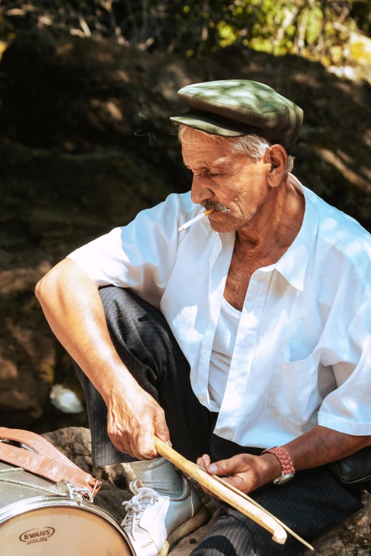 an old man sitting and playing drums on a sunny day