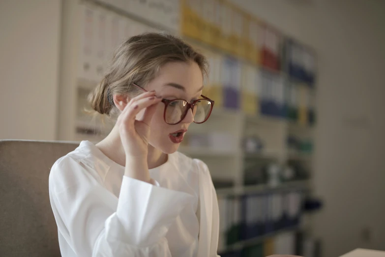 a woman in white shirt holding eyeglasses while looking at computer