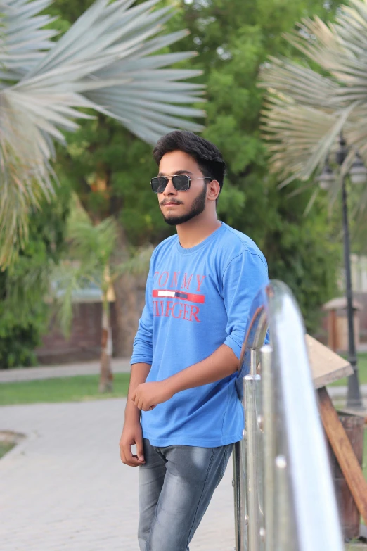 a young man in sunglasses leaning on a fence