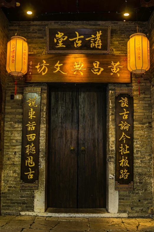 two wooden doors with yellow and gold lettering are decorated by lanterns