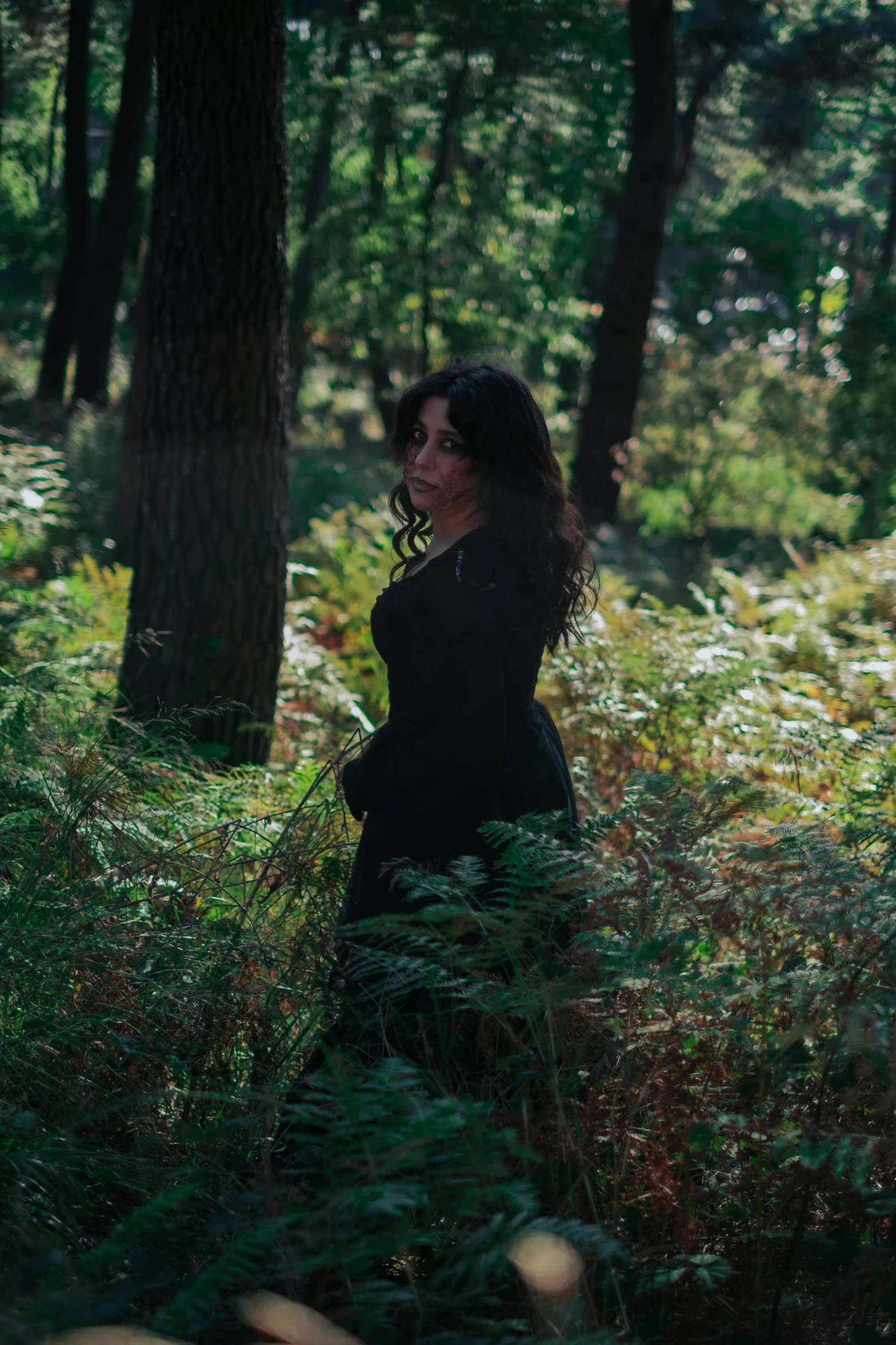 a woman walking through the woods with her hands on her hips