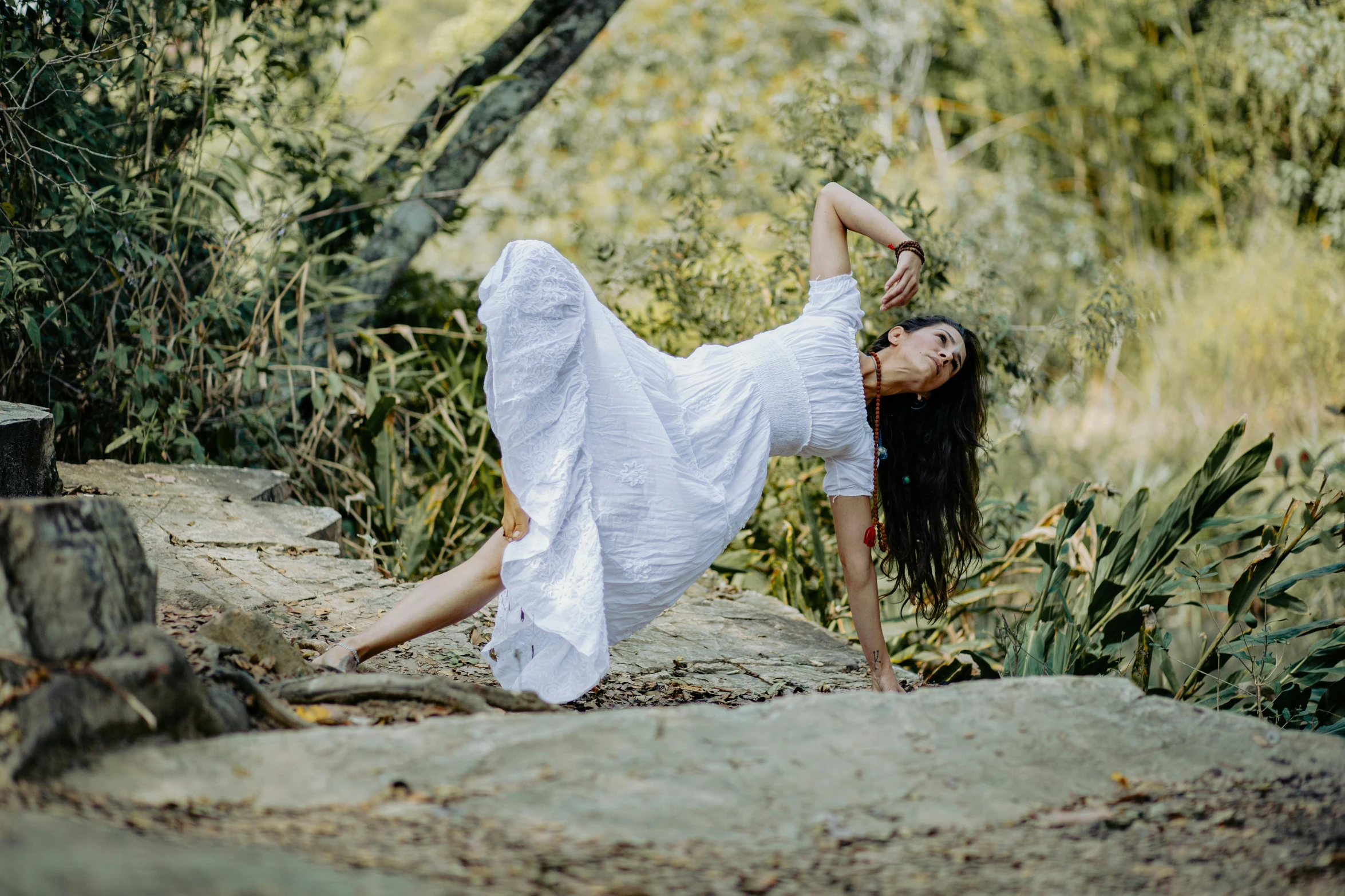 a woman in a white dress dancing near some trees