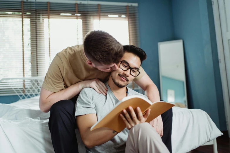 two people sitting on a bed looking at a book