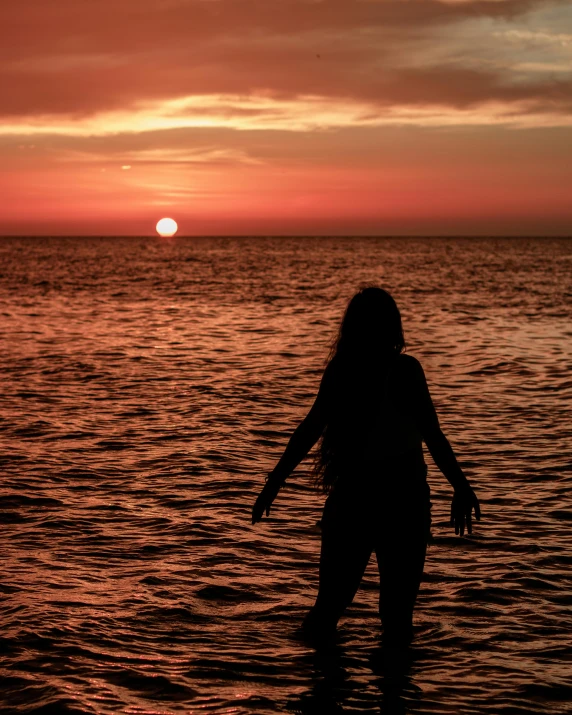 a silhouette of a woman standing on the water at sunset