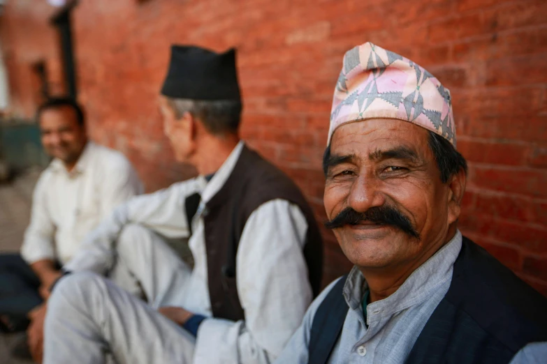 two men smile while sitting against a brick wall