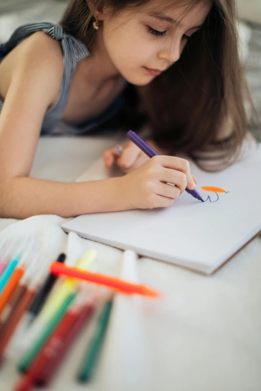 a small girl writes while surrounded by color crayons