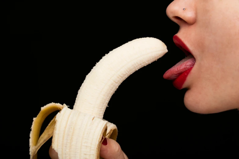 woman taking a bite of banana on her tongue