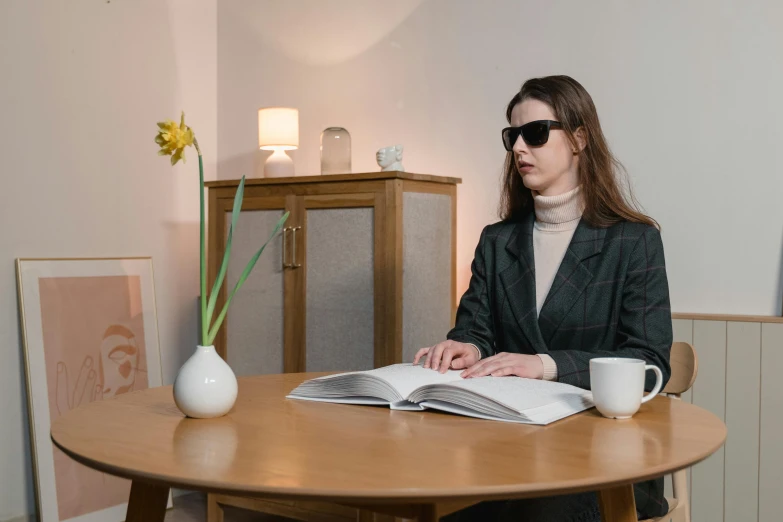 a woman with glasses sitting at a table reading a book