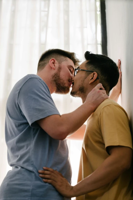 the man is kissing the mans nose in front of a window