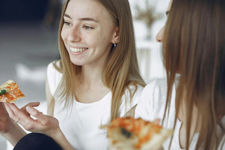 two young women are having a conversation over slices of pizza