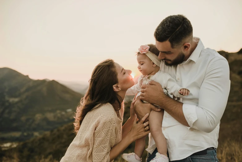 a man holds his baby in one hand and kisses the child's cheek