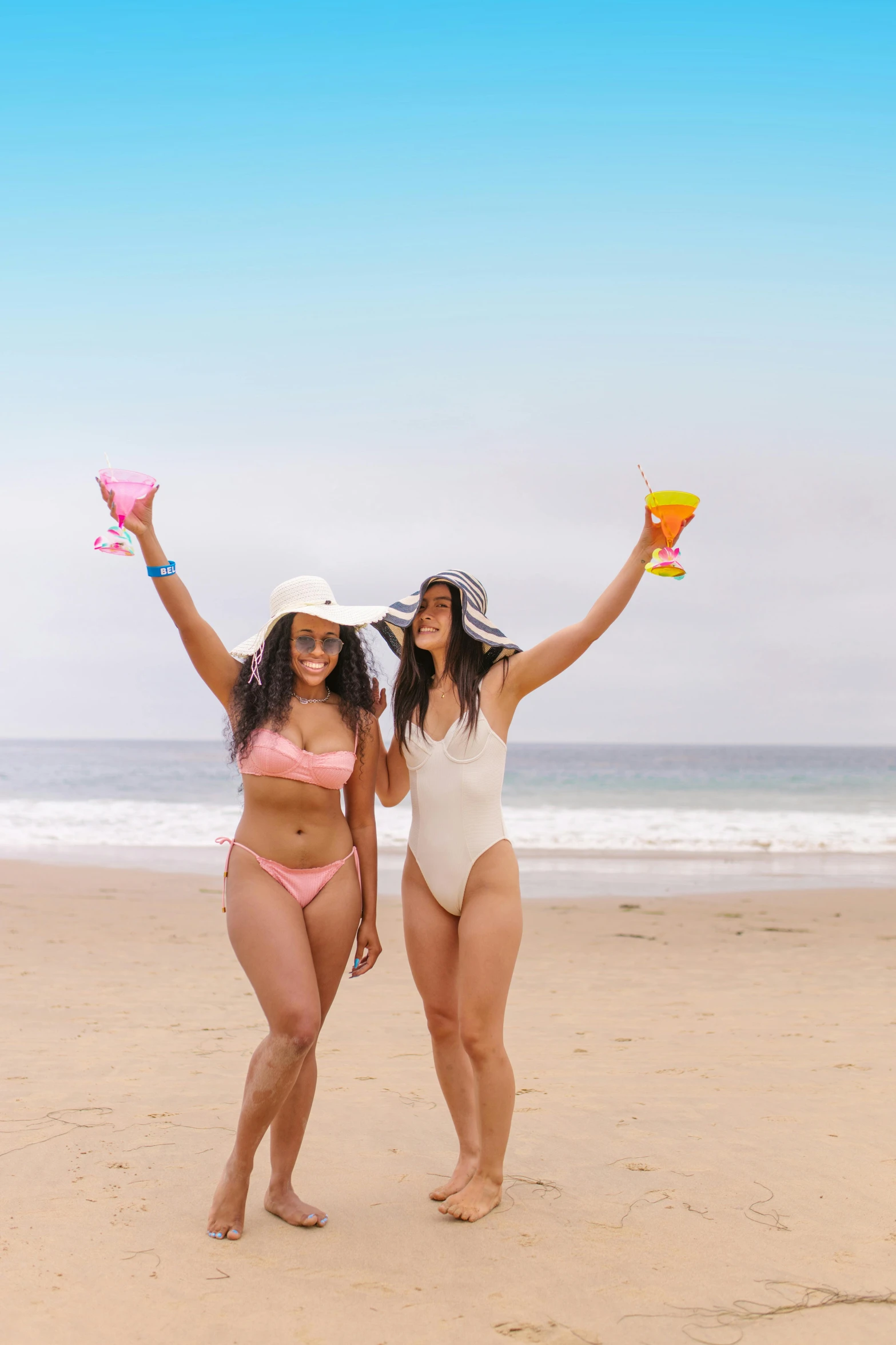 two women standing on the beach holding hats and towels