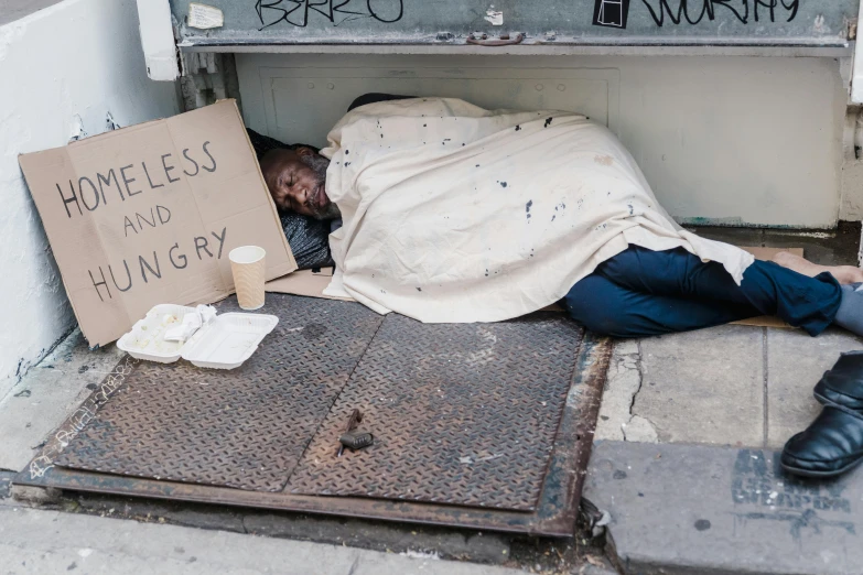 a homeless person lays down with his head on a sign