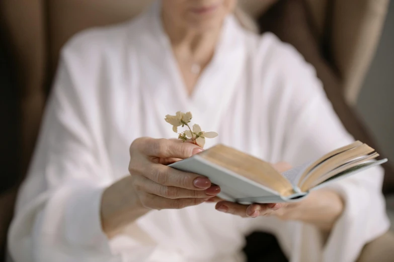 an older woman holding a book with a flower on it