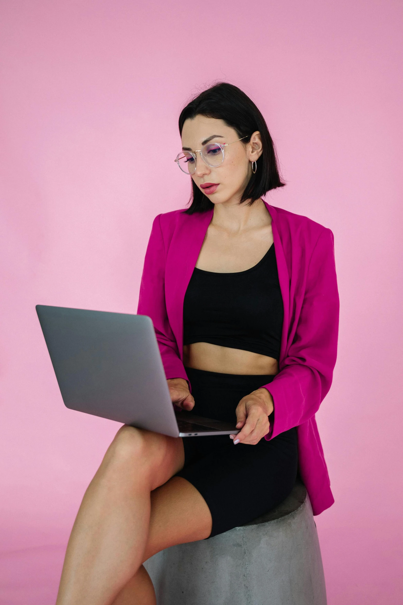 a woman in tight clothing sits on top of a cement ball, holding an open laptop