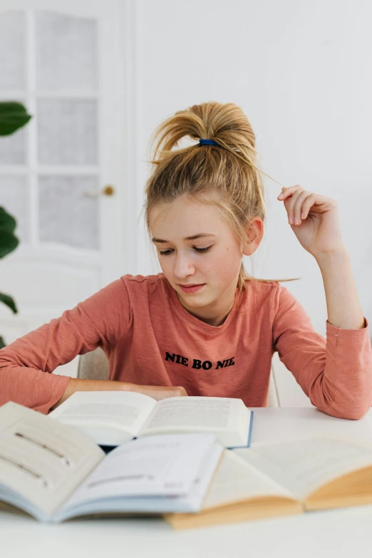 a girl sits at her desk reading a book and touching her hair