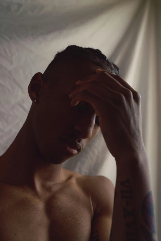 shirtless man looking pensive and holding his hand to his forehead