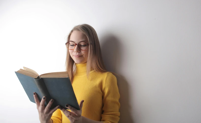 a woman in glasses holding an open book in front of her face