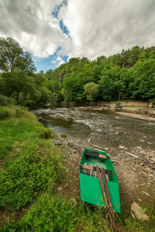 an old green boat sits on shore near the river