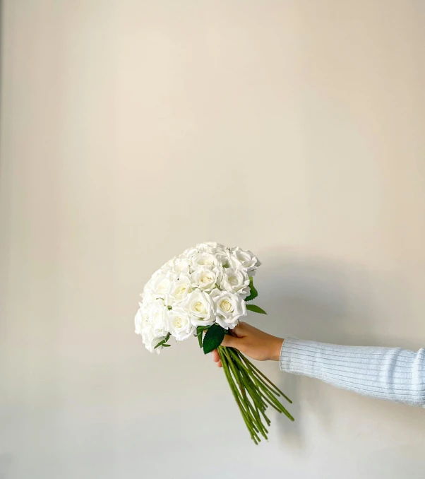 a hand holding a bouquet of white roses