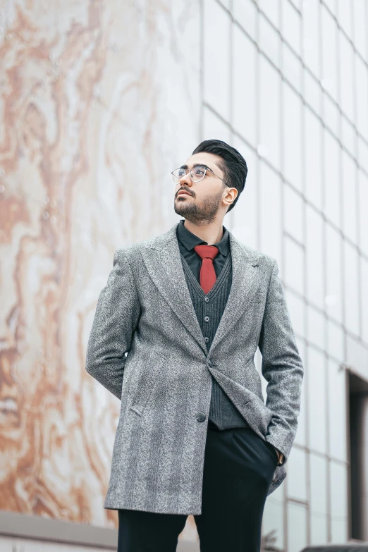 the man is posing in front of the wall wearing a black and red suit