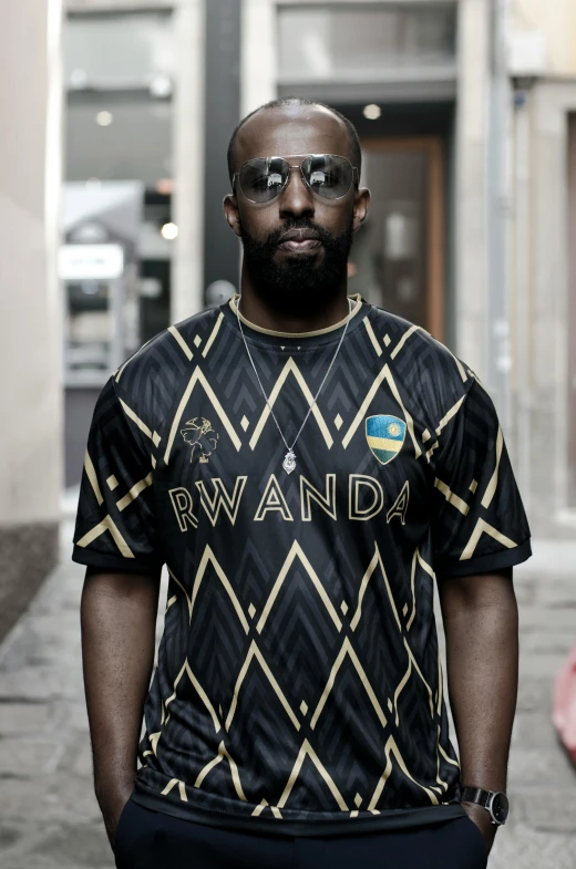 a man stands in front of a building wearing a black and gold shirt