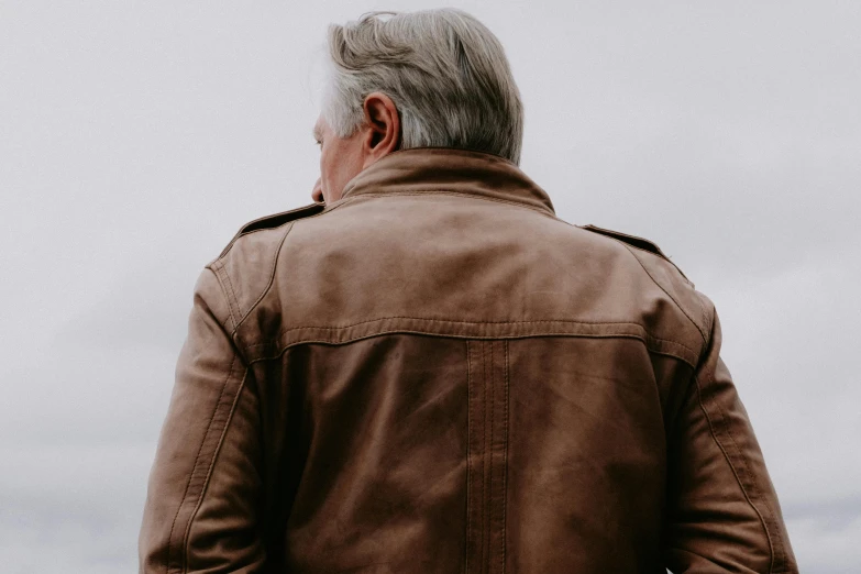 man in brown jacket staring at cloudy sky