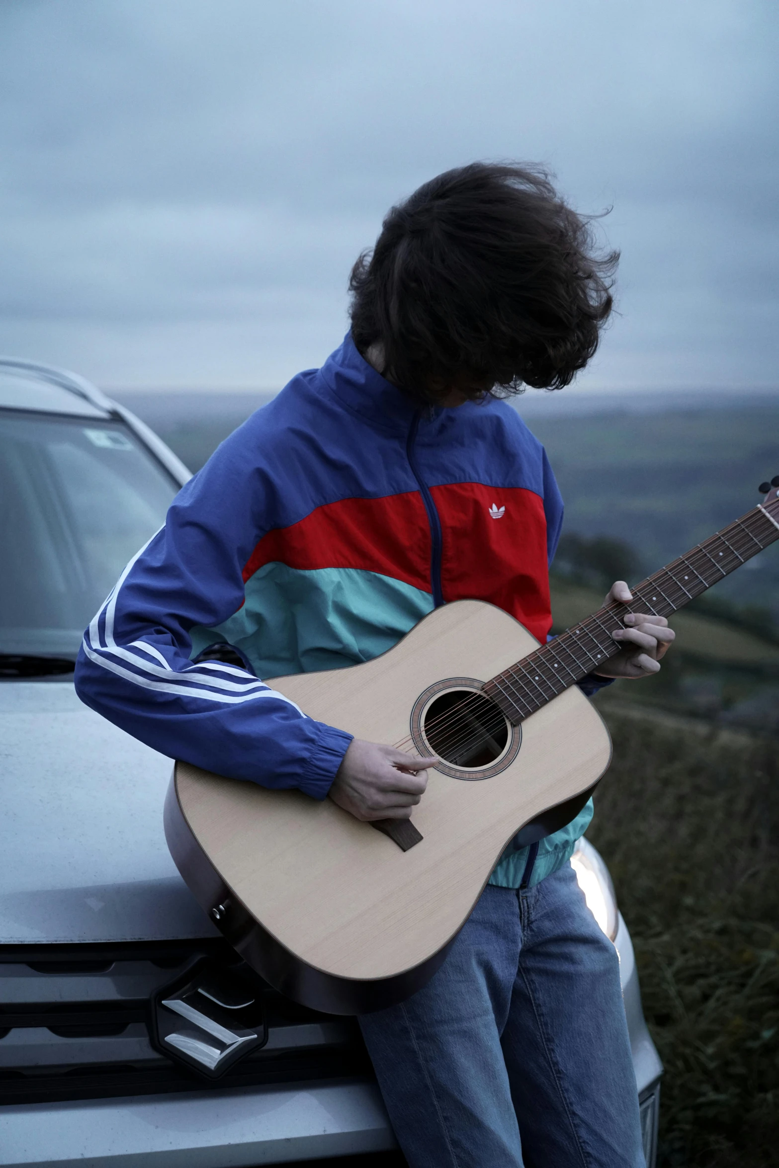 the boy is playing the guitar on the roof of the car