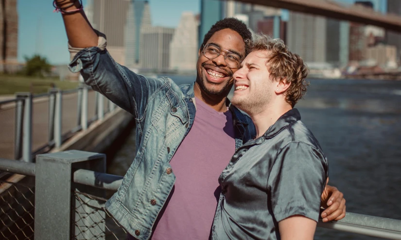 two men smiling and emcing one another, with a bridge in the background