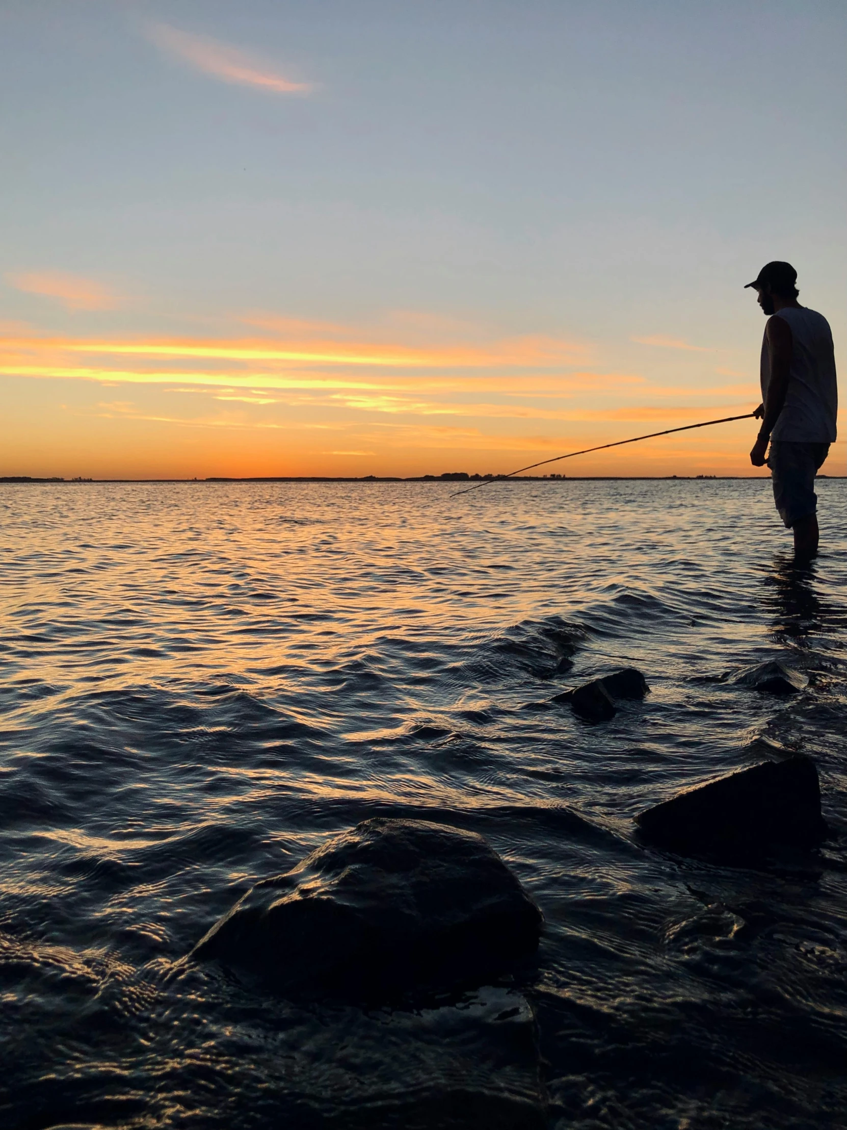 a man standing on the shore of a lake while holding onto a fishing rod