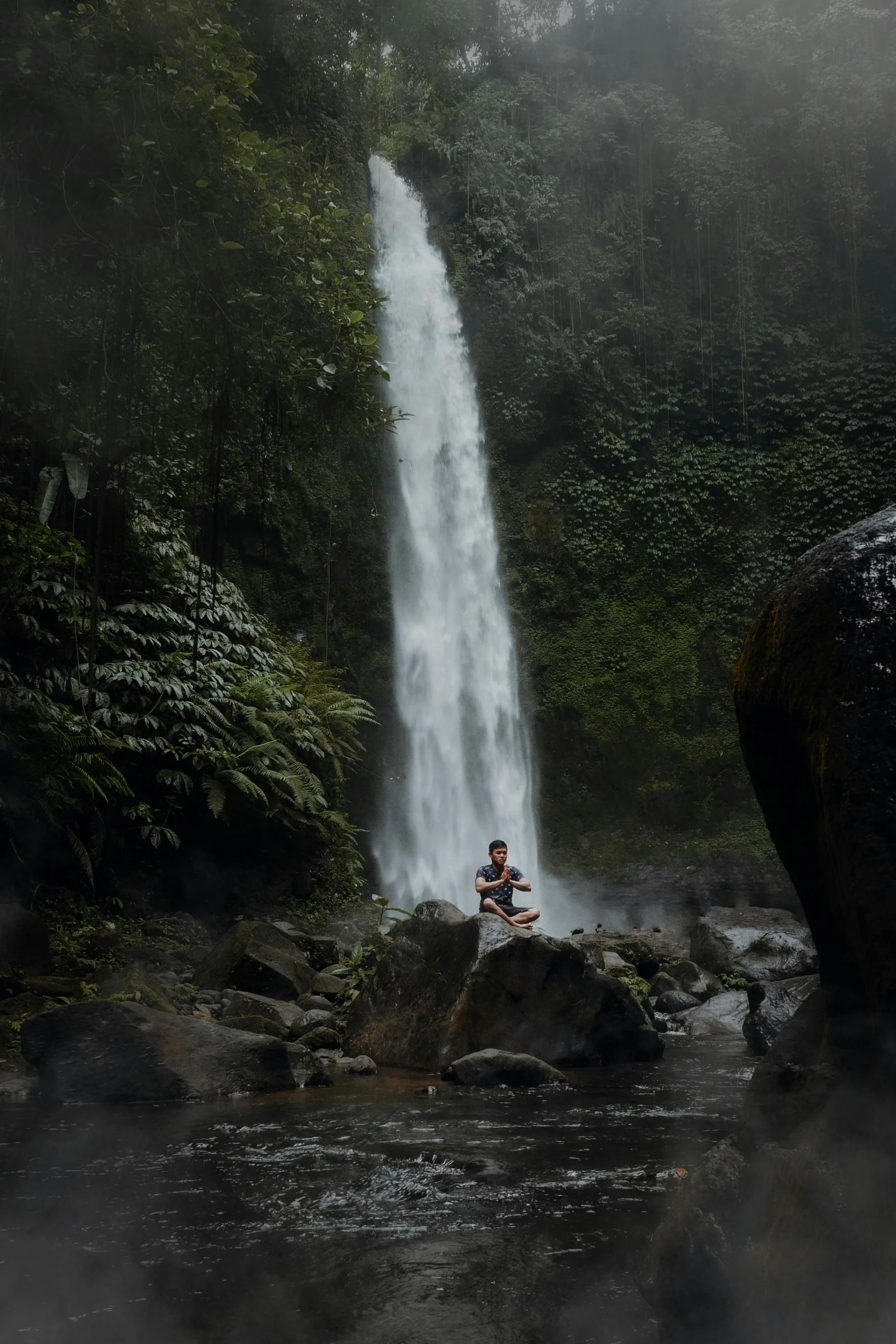 a person is sitting on a rock in front of a waterfall