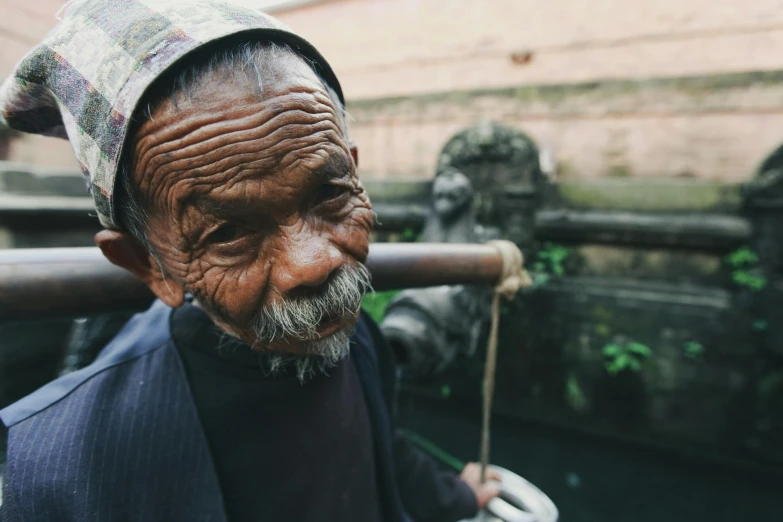 an elderly man with a hat on standing in front of a statue