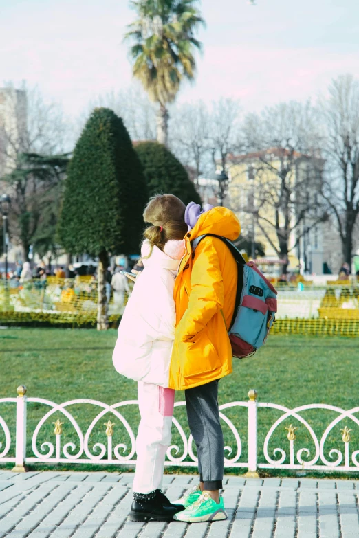 two children in yellow coats standing on sidewalk near gate