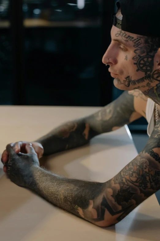 a man with tattoos sitting on the ground looking down