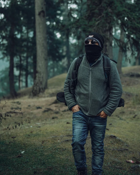 a man wearing a hood and jacket while walking on grass