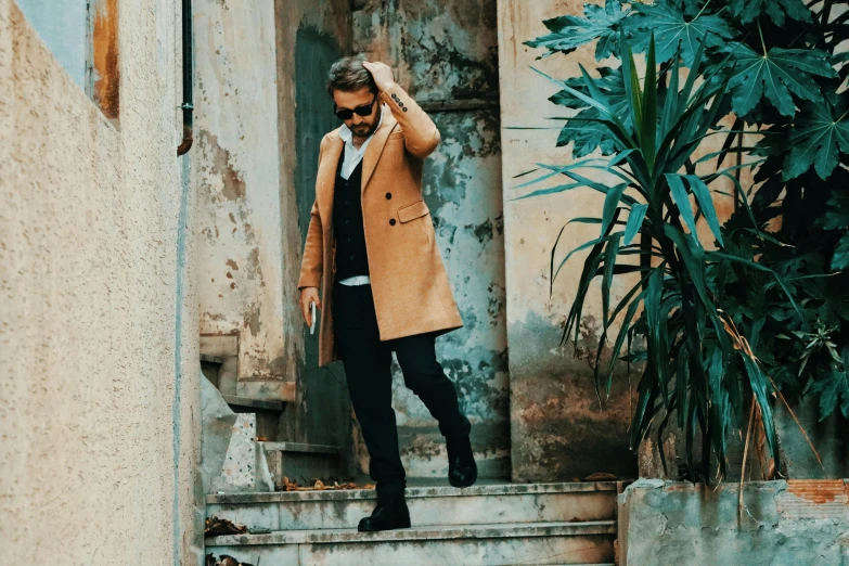 a man in brown coat and sunglasses walking up steps