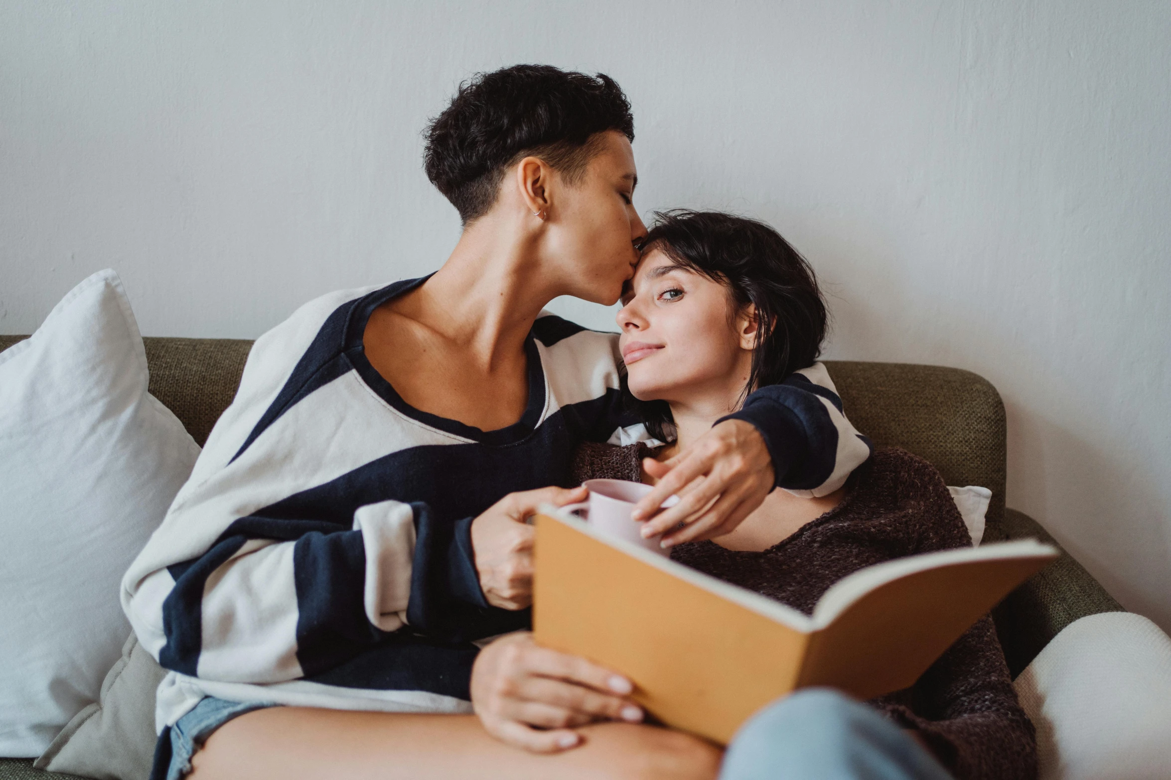 man and woman sitting on a sofa cuddle while reading a book