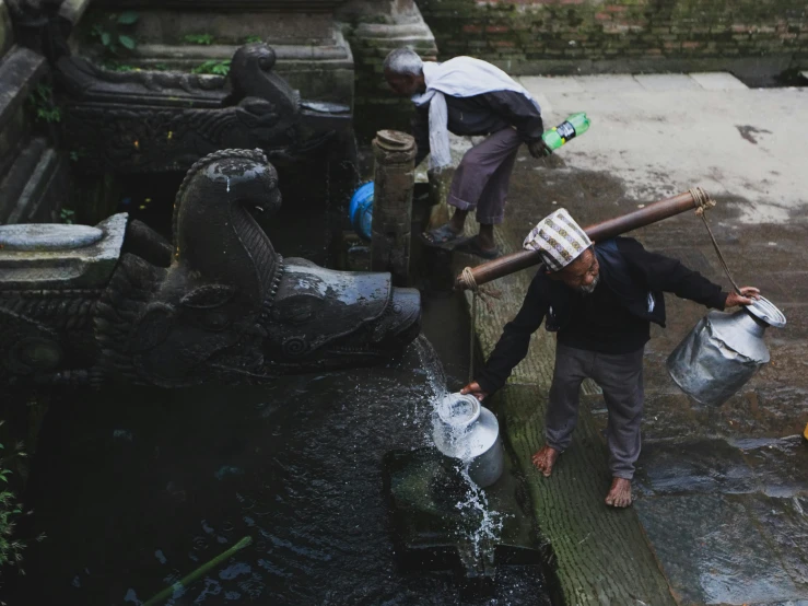 two men are holding up buckets while standing over a pond