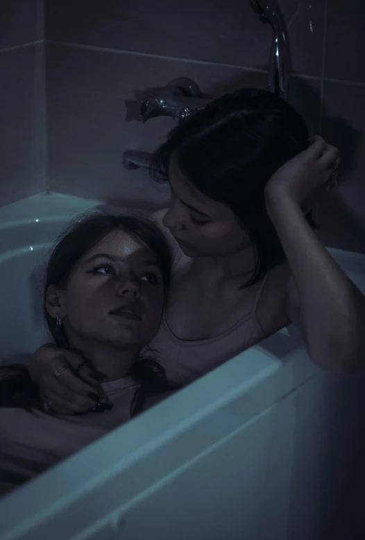 two women with one in the bath tub as the other appears to be thinking about soing