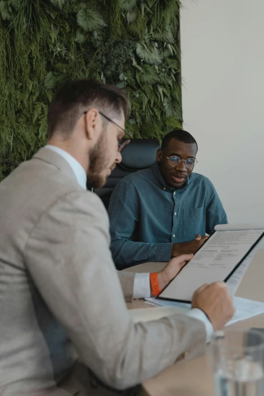 two men in a meeting with a laptop and a binder