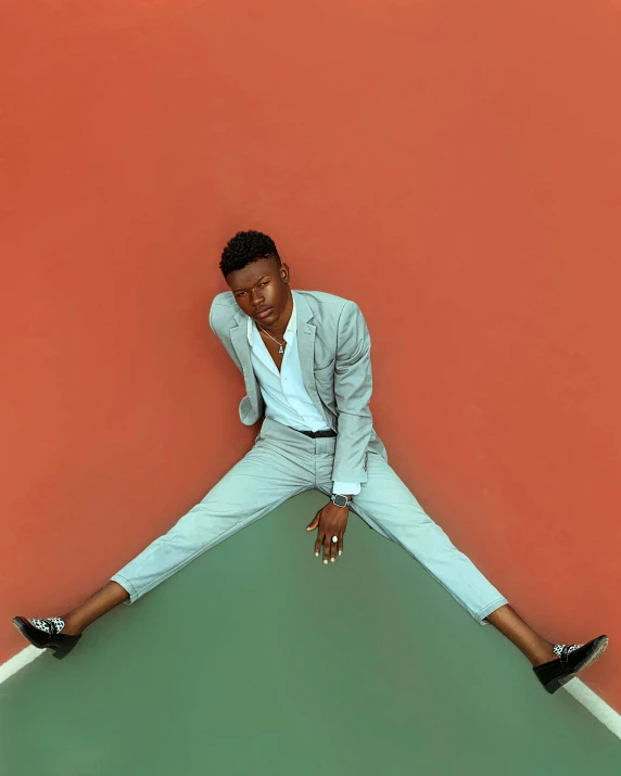 a man in a white shirt, black shoes and a blazer leaning on a wall