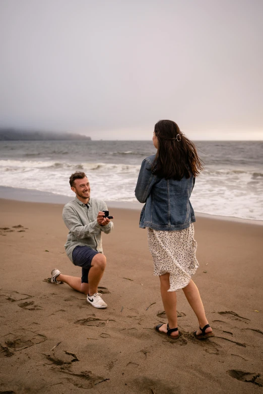 a woman kneeling down and another man taking a pograph on the beach